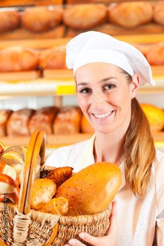 Photo: Female baker in bakery selling bread by basket Female baker in bakery selling bread by basket