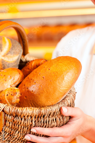 Photo: Female baker in bakery selling bread by basket Female baker in bakery selling bread by basket