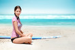 Foto: Sexy surf girl sitting on beach with surfboard and relaxing Sexy surf girl sitting on beach with surfboard and relaxing