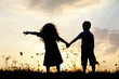 Silhouette, group of happy children playing on meadow, sunset