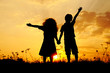 Silhouette, group of happy children playing on meadow, sunset