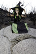 Little young girl costumed as witch sitting on rock looking away