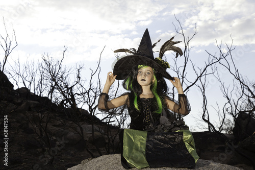 Foto: Girl sitting on rock stone holding her witch hat Girl sitting on rock stone holding her witch hat