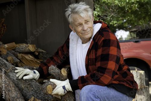Foto: Senior man sitting besides firewood log Senior man sitting besides firewood log
