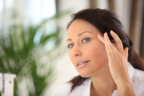 Photo: a woman spreading out cosmetic cream on her face a woman spreading out cosmetic cream on her face