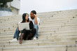 Young people sitting on steps of stairs with laptop