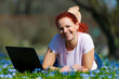 rothaarige frau liegt mit notebook im gras