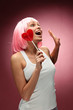 Young girl in pink wig with lollipop posing on a pink background