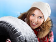 Foto: Pretty young woman behind a snowy winter tyre Pretty young woman behind a snowy winter tyre