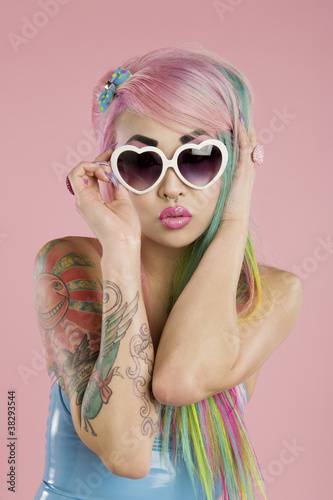 Photo: Young woman posing wearing sunglasses over pink background Young woman posing wearing sunglasses over pink background