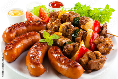 Photo: Grilled meat, sausages and vegetables on white background Grilled meat, sausages and vegetables on white background