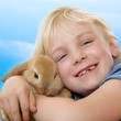Foto: Cute blonde girl is cuddling with her little rabbit outdoors Cute blonde girl is cuddling with her little rabbit outdoors