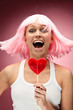 Young girl in pink wig with lollipop posing on a pink background