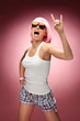 Young girl in pink wig and glasses dancing on a pink background
