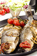 two grilled sea bass in a pan with tomato and onion
