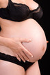 Pregnant woman touching her belly with hands, dark barkground
