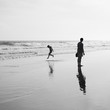 small boy plays by the ocean as his dad watches on