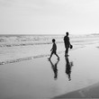 small boy plays by the ocean as his dad watches on