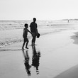 small boy plays by the ocean as his dad watches on