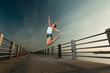 Young woman jumping in sunset light on a pier