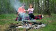 Boy and girl sit on log and watch at bonfire burn