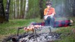 Boy sit on log and drink juice, meat cooking on embers