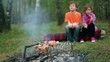 Boy and girl sit on log and watch at fresh meat on embers