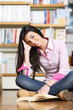 smiling female college student sitting on floor in library, read