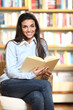 smiling female student with book in hands sitting in a chair in