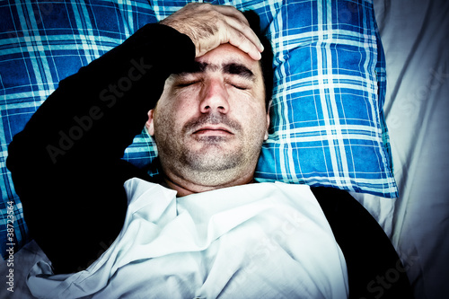 Photo: Very stressed man with a headache laying in bed Very stressed man with a headache laying in bed