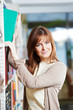 Smiling young adult woman reading  book in library