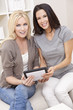 Two Young Women Using Tablet Computer At Home on Sofa