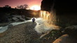 Child watching a waterfall and tossing a rock at sunset in Kenya.