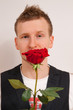 junger Mann haelt rote Rose in Hand