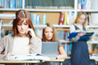 Smiling young adult woman reading  book in library