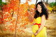 Beautiful pregnant woman with red band on belly, autumn outdoors