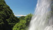 滝の水しぶきと新緑の森と青空