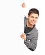 A smiling handsome male posing behind a white panel