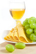 A glass of white wine, sliced cheese and green grapes on wood