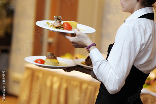 Photo: Waitress is carrying three plates with meat dish Waitress is carrying three plates with meat dish