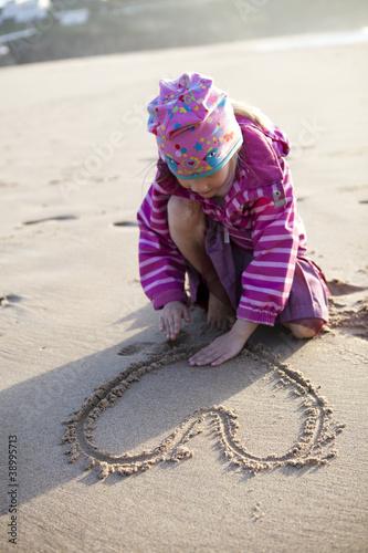 Foto: Girl drawing a heart in sand Girl drawing a heart in sand