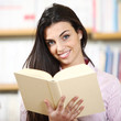 smiling female student with book in hands in a bookstore - model