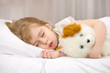 Little girl sleeping in bed with a soft toy.