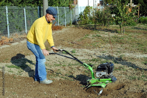 Photo: Middle age man with a rototiller in the garden Middle age man with a rototiller in the garden