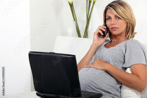 Photo: Pregnant woman sitting on the sofa with a laptop and telephone Pregnant woman sitting on the sofa with a laptop and telephone
