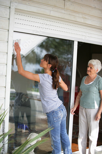 Photo: Woman cleaning a glass patio door for an elderly lady Woman cleaning a glass patio door for an elderly lady