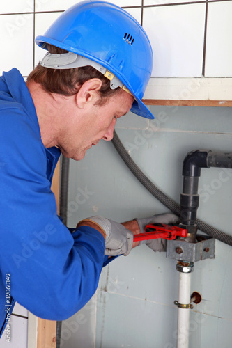 Photo: Man installing water pipes with a large wrench Man installing water pipes with a large wrench