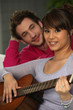 a man looking a woman playing guitar