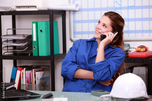 Photo: Young woman in blue overalls on the telephone in a depot Young woman in blue overalls on the telephone in a depot