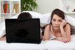 Unimpressed woman in bed with her partner and his laptop